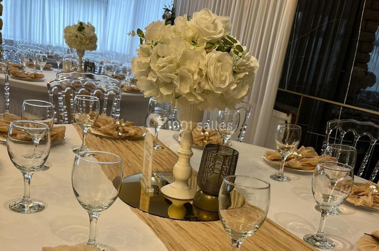 Centre de table avec fleurs blanches sur une table dressée, entourée de chaises transparentes dans une salle lumineuse.