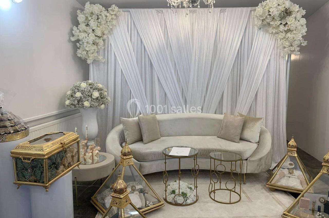 Salon décoré dans des tons blancs et dorés, avec un canapé, des tables dorées et des présentoirs ornés de fleurs.