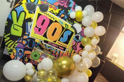 Mur décoratif sur le thème des années 90 avec graffitis colorés, ballons blancs et dorés, et accessoires rétro.