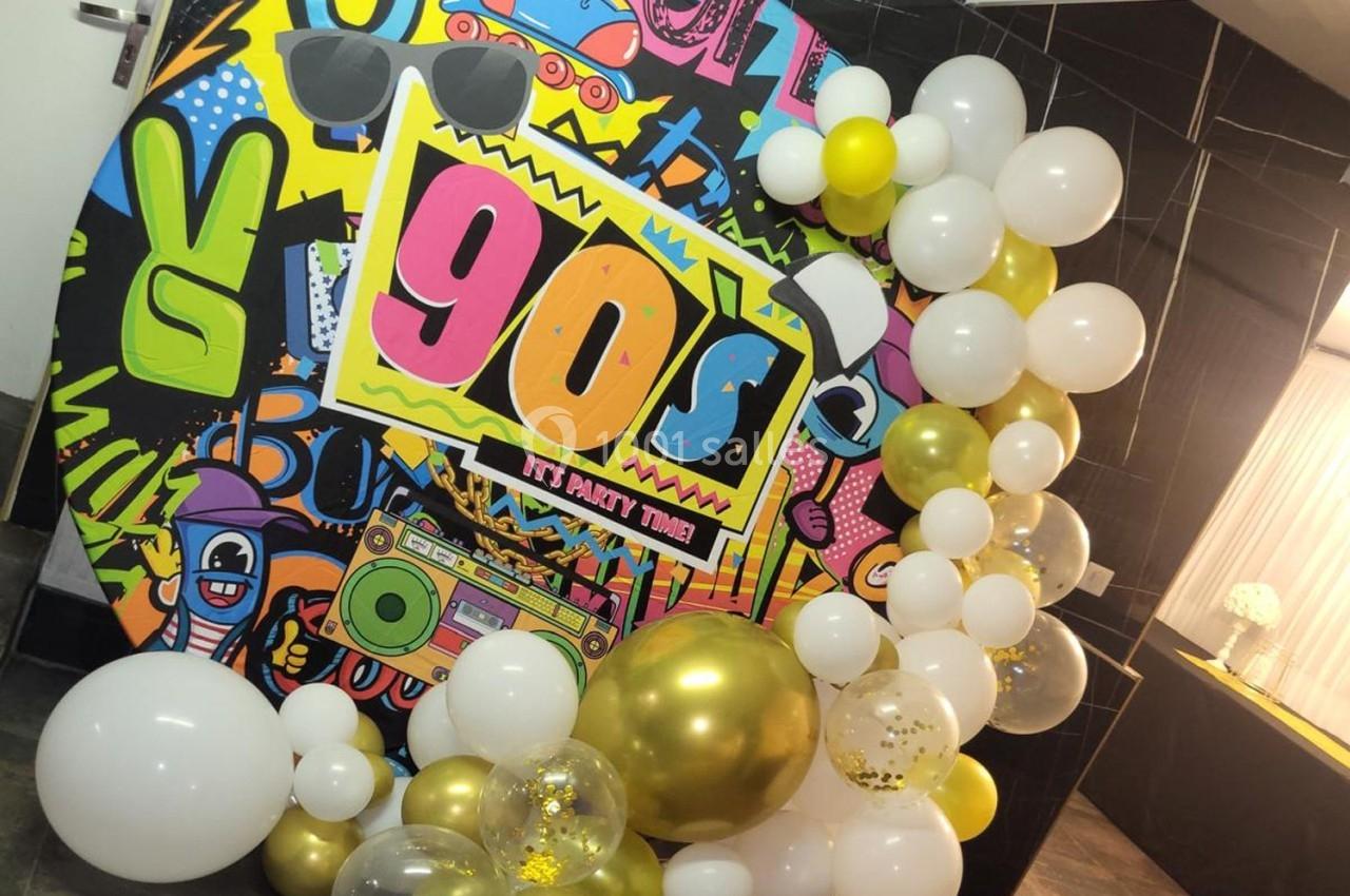 Mur décoratif sur le thème des années 90 avec graffitis colorés, ballons blancs et dorés, et accessoires rétro.