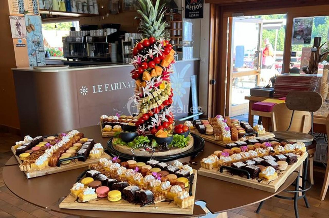 Plateau central de fruits décoratifs entouré de planches de pâtisseries variées dans un café lumineux.