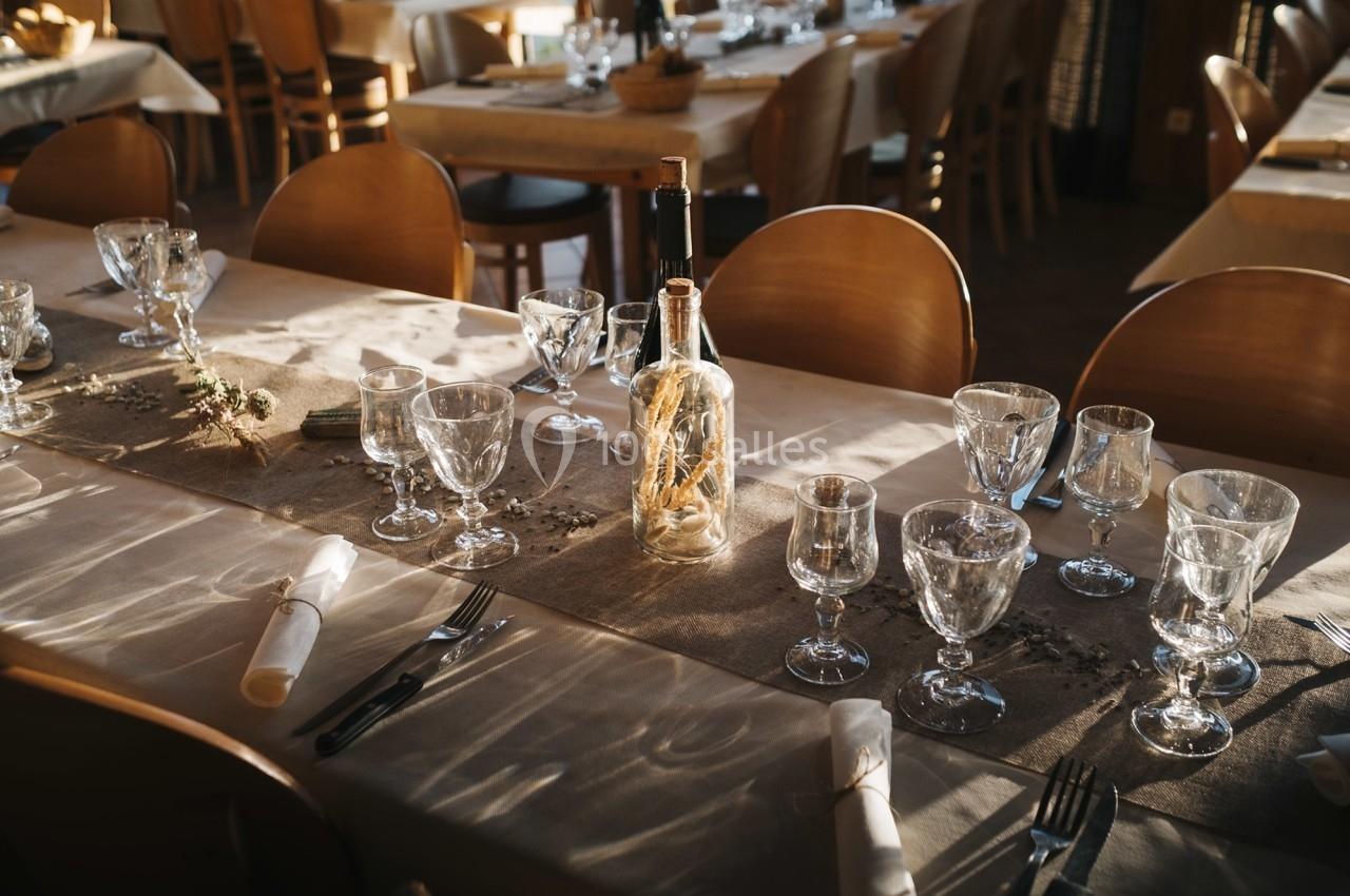 Table dressée avec nappes blanches, verres, couverts et une bouteille décorative au centre, dans une salle lumineuse.