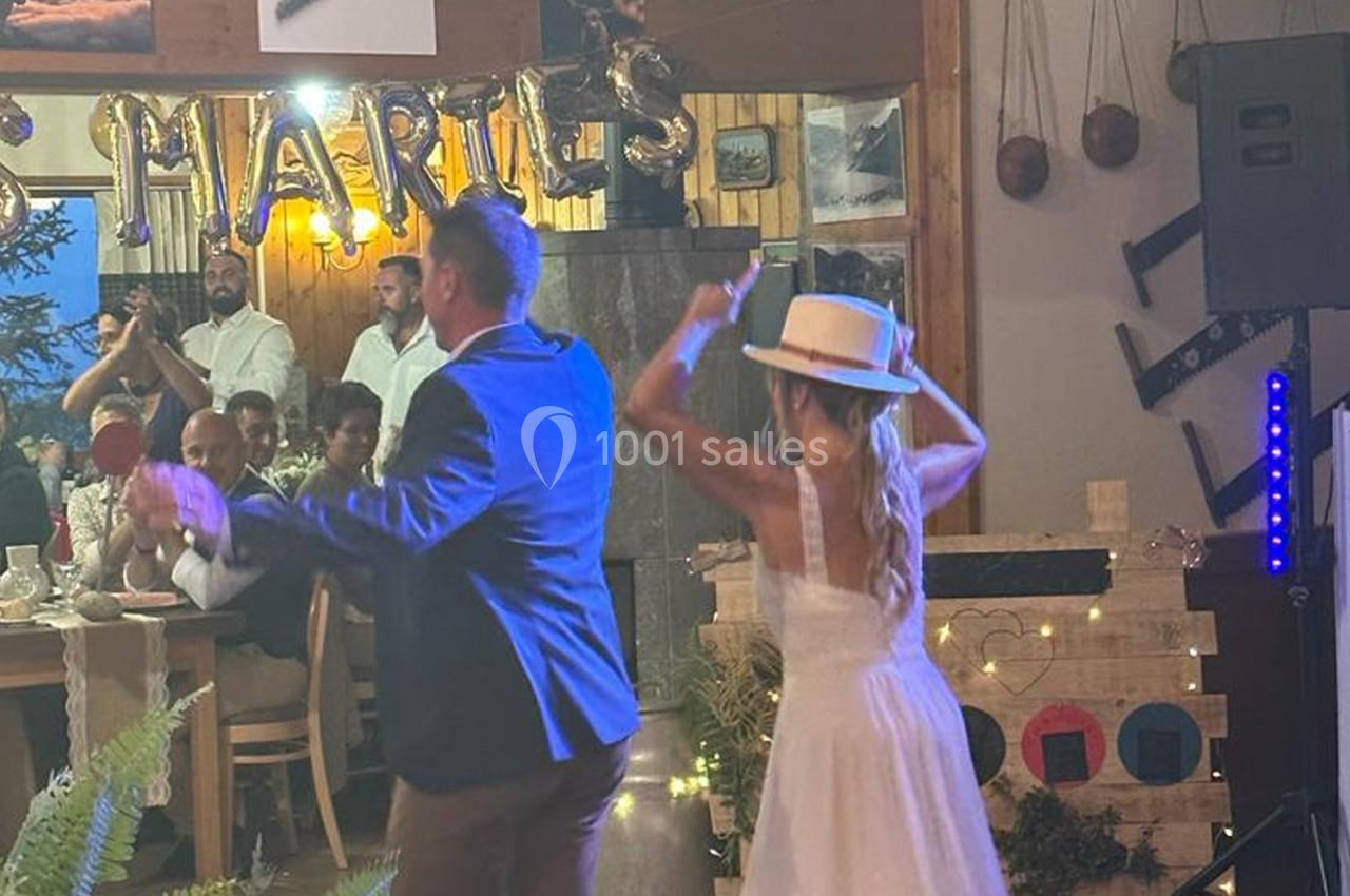 Un couple danse dans une salle décorée, entouré d'invités assis à des tables lors d'une fête.