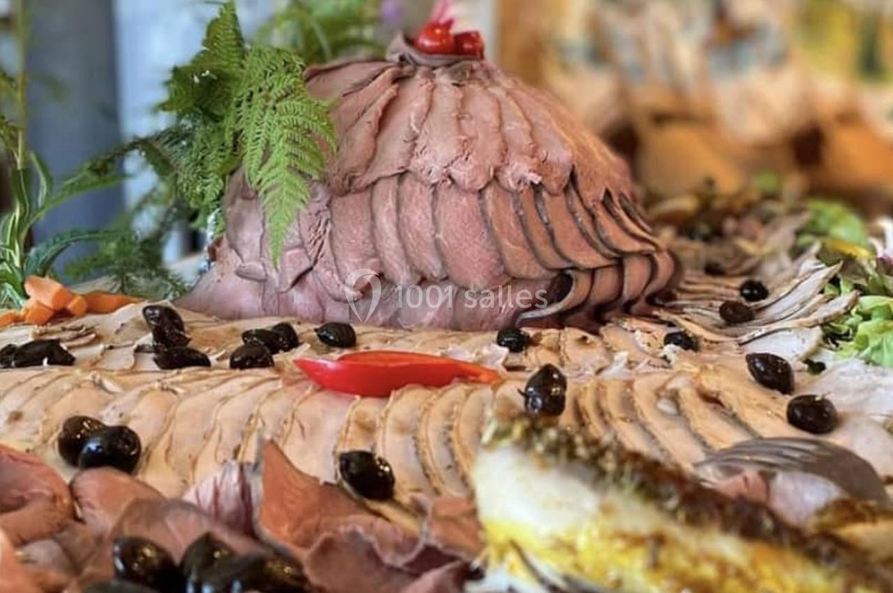 Plateau de charcuterie avec tranches de viande disposées en éventail, olives noires et garniture de légumes.