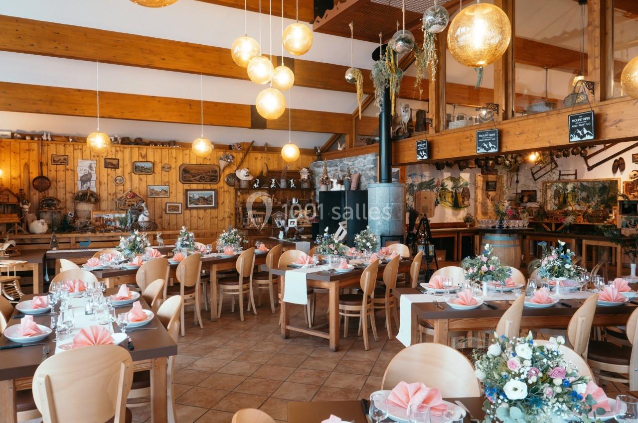 Salle de restaurant décorée avec des tables dressées, nappes roses, bouquets de fleurs et éclairage chaleureux.
