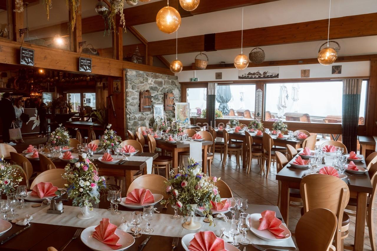Salle de réception décorée avec des tables dressées, nappes blanches, serviettes pliées rouges et bouquets de fleurs.