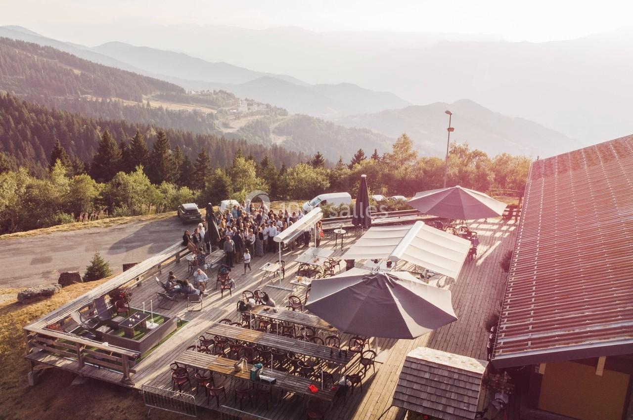 Terrasse en bois d'un restaurant en montagne avec des tables, des parasols et une vue panoramique sur la vallée.