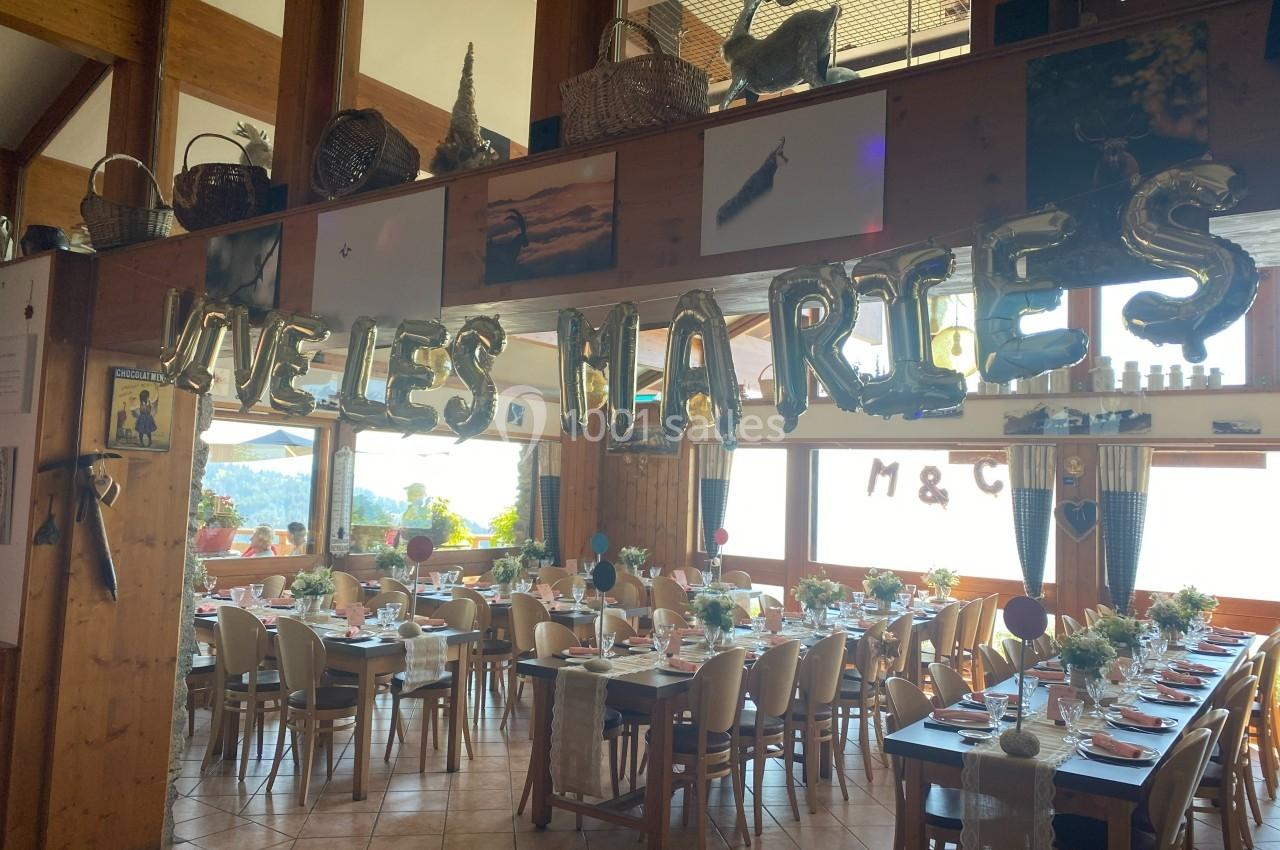 Salle décorée pour un mariage avec des ballons formant ’Vive les mariés’, tables dressées et vue sur l'extérieur lumineux.
