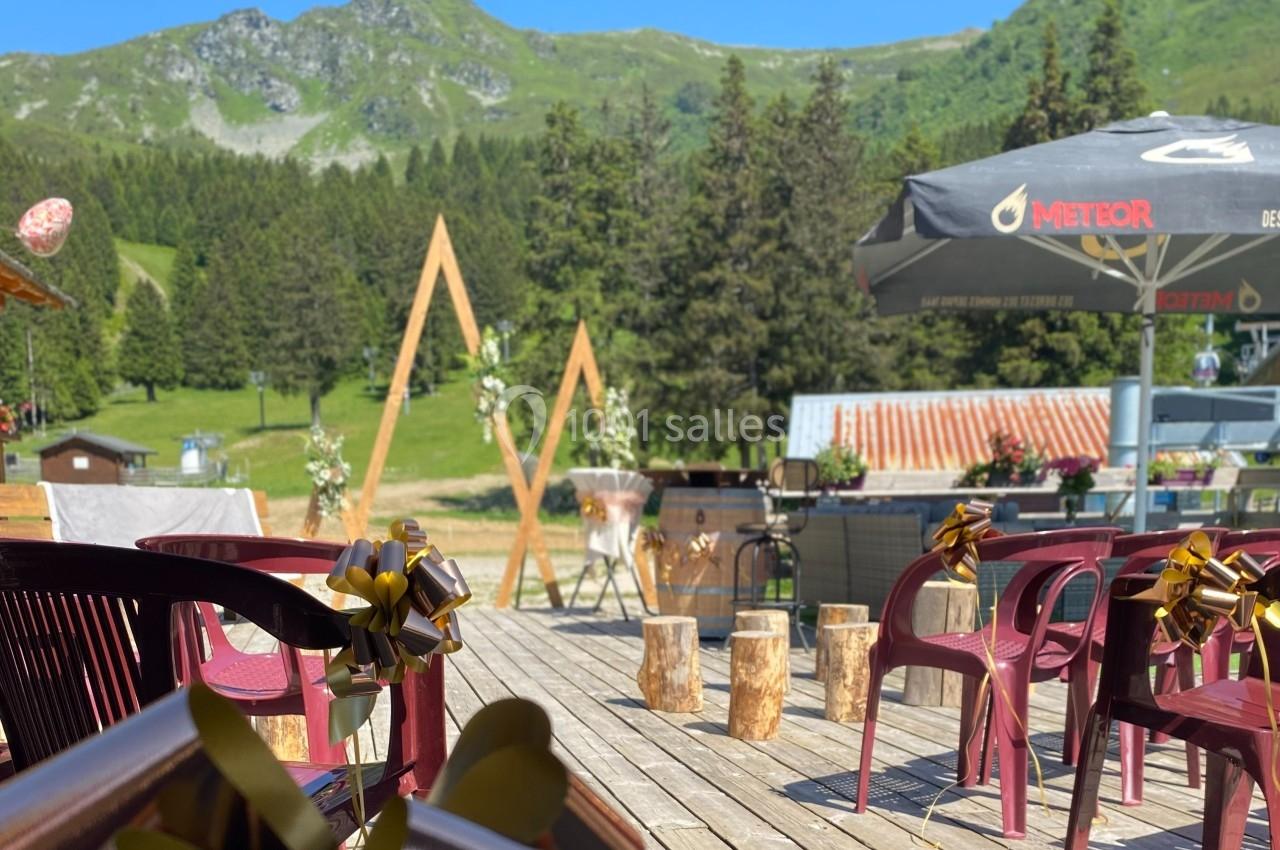 Chaises décorées et arche en bois installées sur une terrasse en montagne, entourées de verdure et de sapins.