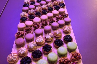 Plateau en bois garni de macarons colorés, tartelettes aux fruits et pâtisseries variées disposés en rangées.