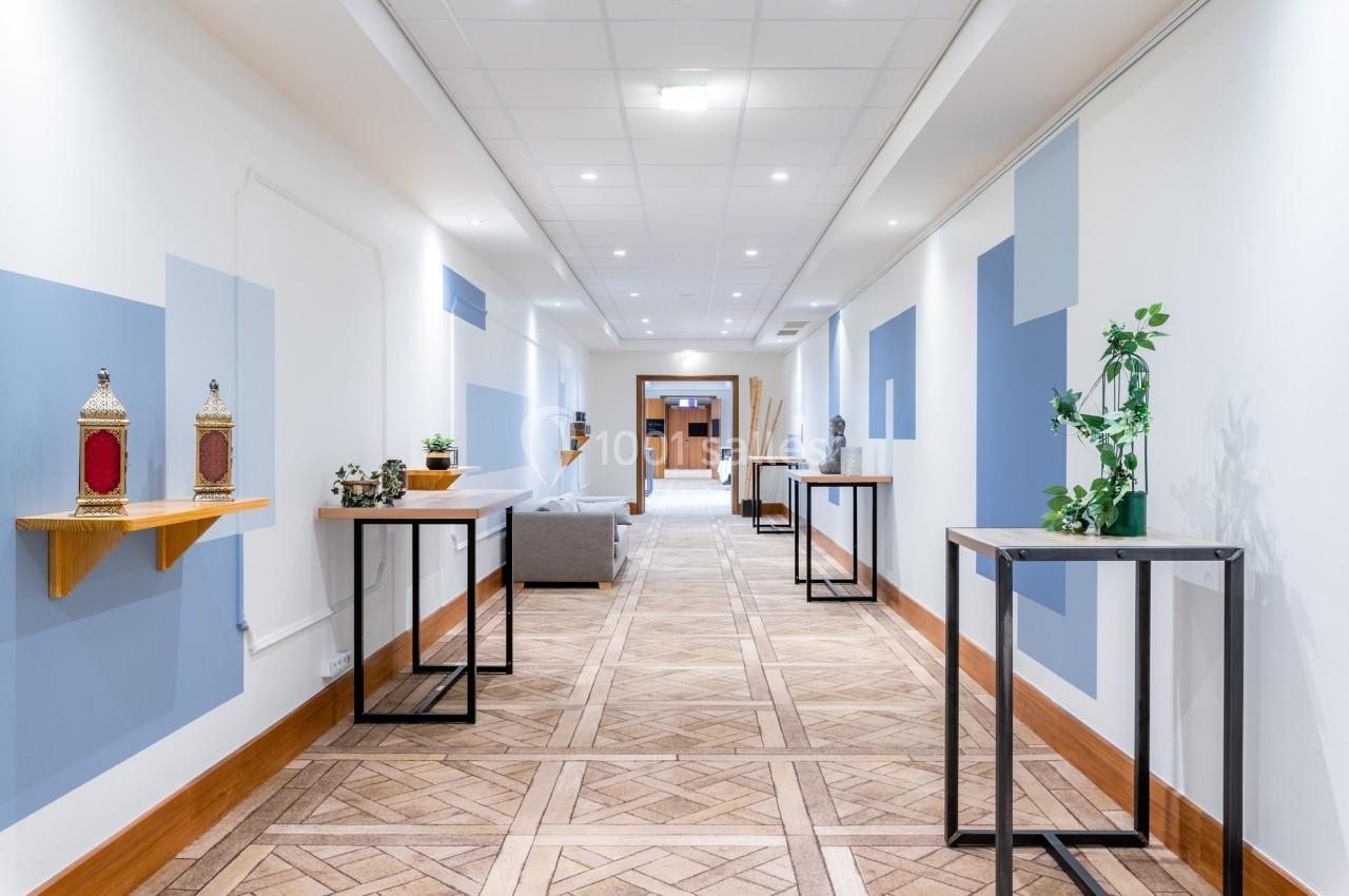 Couloir lumineux avec sol en parquet, murs décorés de motifs bleus et étagères portant des objets décoratifs.