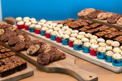 Chambre d'hôtel lumineuse avec lit double, coin salon, rideaux jaunes, mobilier en bois et fauteuils bleus.