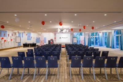Chambre d'hôtel lumineuse avec lit double, coin salon, rideaux jaunes, mobilier en bois et fauteuils bleus.
