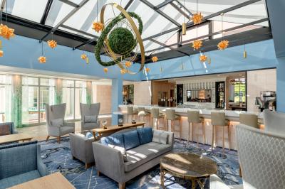 Chambre d'hôtel lumineuse avec lit double, coin salon, rideaux jaunes, mobilier en bois et fauteuils bleus.