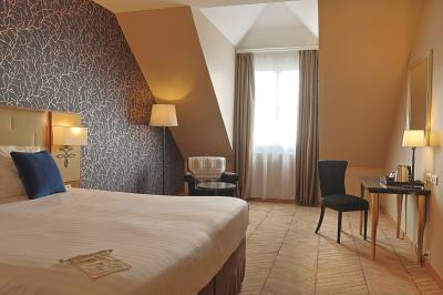 Chambre d'hôtel lumineuse avec lit double, coin salon, rideaux jaunes, mobilier en bois et fauteuils bleus.