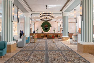 Chambre d'hôtel lumineuse avec lit double, coin salon, rideaux jaunes, mobilier en bois et fauteuils bleus.