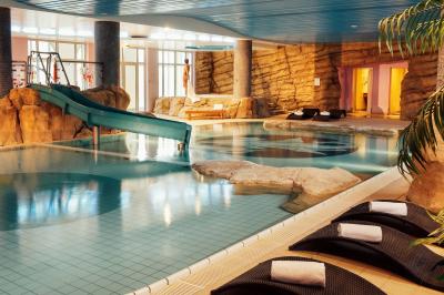 Chambre d'hôtel lumineuse avec lit double, coin salon, rideaux jaunes, mobilier en bois et fauteuils bleus.