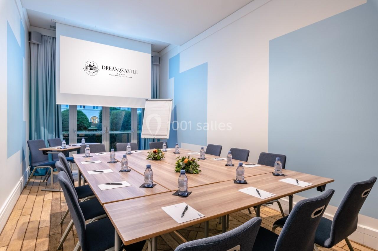 Salle de réunion lumineuse avec table en bois, chaises, bloc-notes, bouteilles d'eau et écran de projection.