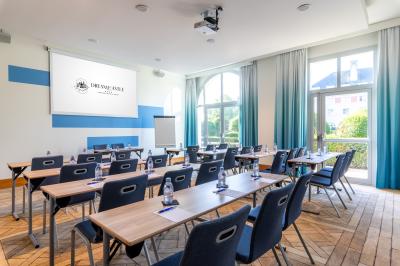 Chambre d'hôtel lumineuse avec lit double, coin salon, rideaux jaunes, mobilier en bois et fauteuils bleus.