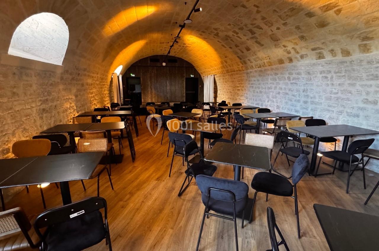 Salle voûtée en pierre avec des tables et des chaises modernes disposées sur un sol en bois.