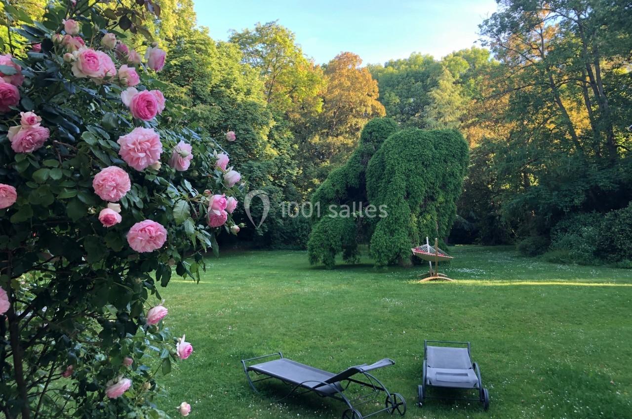 Jardin verdoyant avec rosiers en fleurs, transats sur la pelouse et hamac suspendu sous un arbre.