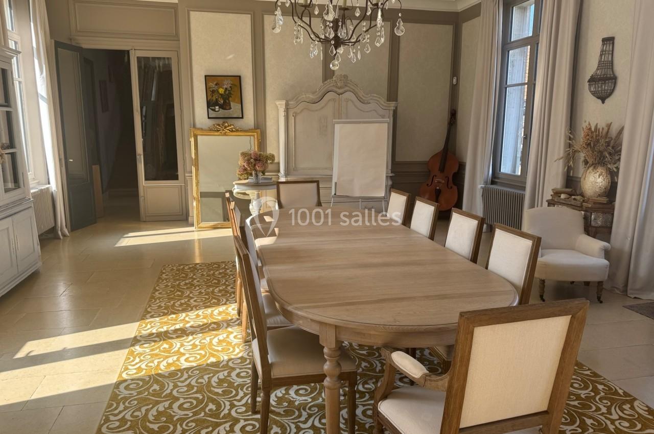 Salle à manger lumineuse avec une grande table en bois, chaises assorties, lustre, et décoration classique.