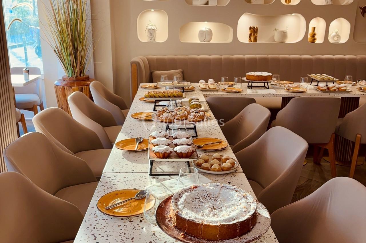 Table dressée avec des desserts variés dans un intérieur lumineux, décoré d'étagères murales et de luminaires suspendus.