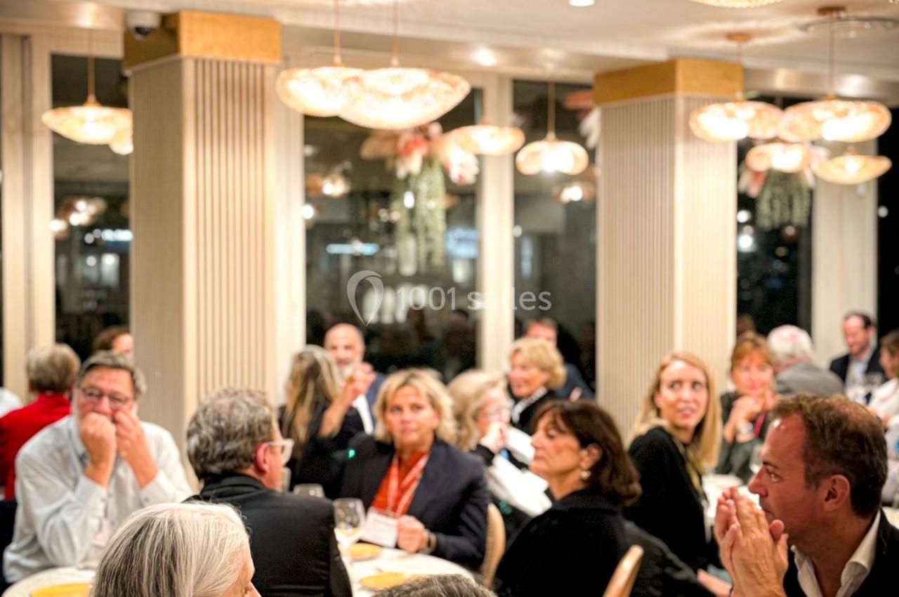 Des convives assis autour de tables dans un restaurant élégant, éclairé par des suspensions lumineuses.