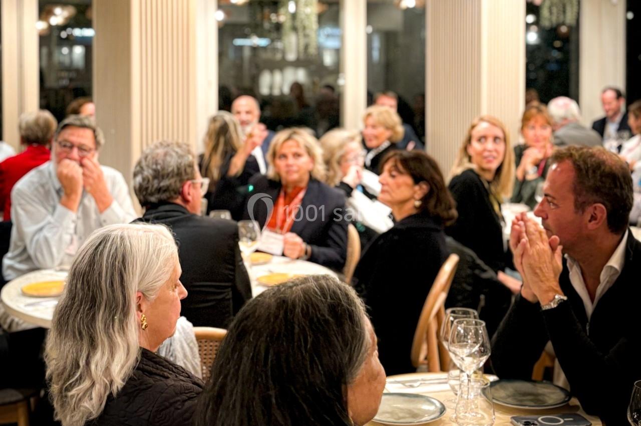 Des personnes assises autour de tables dans une salle éclairée, participant à un événement ou un dîner.