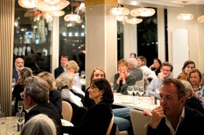 Des personnes assises à des tables dans un restaurant, discutant et partageant un repas dans une ambiance conviviale.