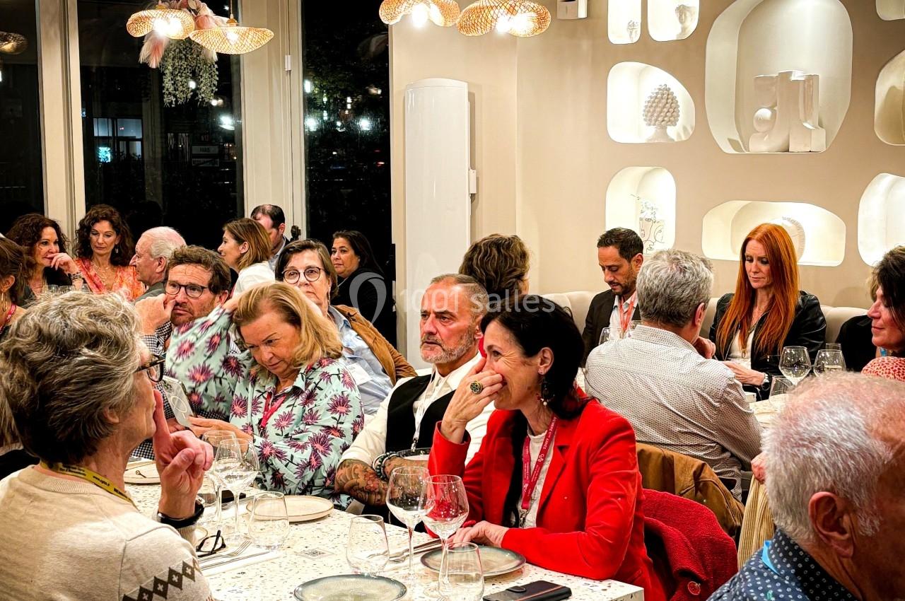 Des personnes assises à des tables dans un restaurant, discutant et partageant un repas dans une ambiance conviviale.