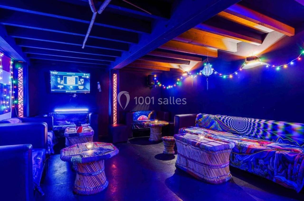 Salle colorée avec éclairage tamisé, guirlandes lumineuses, canapés et tables basses dans une ambiance conviviale.