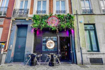 Façade d'un bar avec une décoration végétale, des néons roses et des tabourets noirs sur le trottoir.