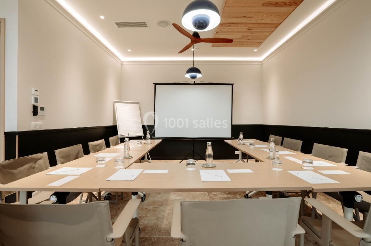 Salle de réunion moderne avec table rectangulaire, chaises, écran de projection, paperboard et bouteilles d'eau.