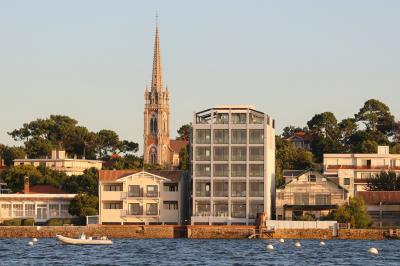 Piscine intérieure avec eau sombre, transats blancs, murs en bois et pierre, et une personne en peignoir flouement visible.