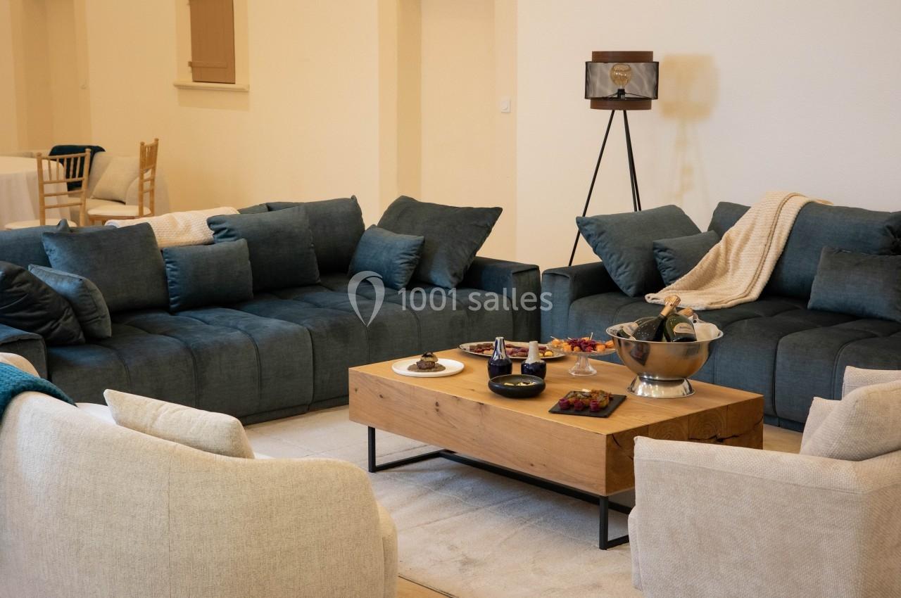 Salon avec deux canapés bleus, deux fauteuils beiges, une table basse en bois et des collations disposées dessus.