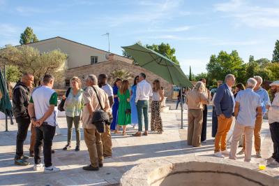 Terrasse couverte en bois avec mobilier d'extérieur blanc, donnant sur un jardin arboré et une allée gravillonnée.