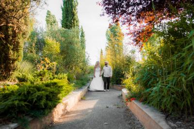 Terrasse couverte en bois avec mobilier d'extérieur blanc, donnant sur un jardin arboré et une allée gravillonnée.