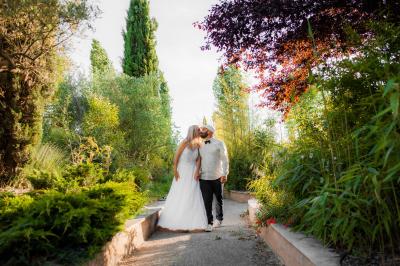 Terrasse couverte en bois avec mobilier d'extérieur blanc, donnant sur un jardin arboré et une allée gravillonnée.