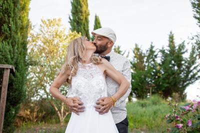 Terrasse couverte en bois avec mobilier d'extérieur blanc, donnant sur un jardin arboré et une allée gravillonnée.