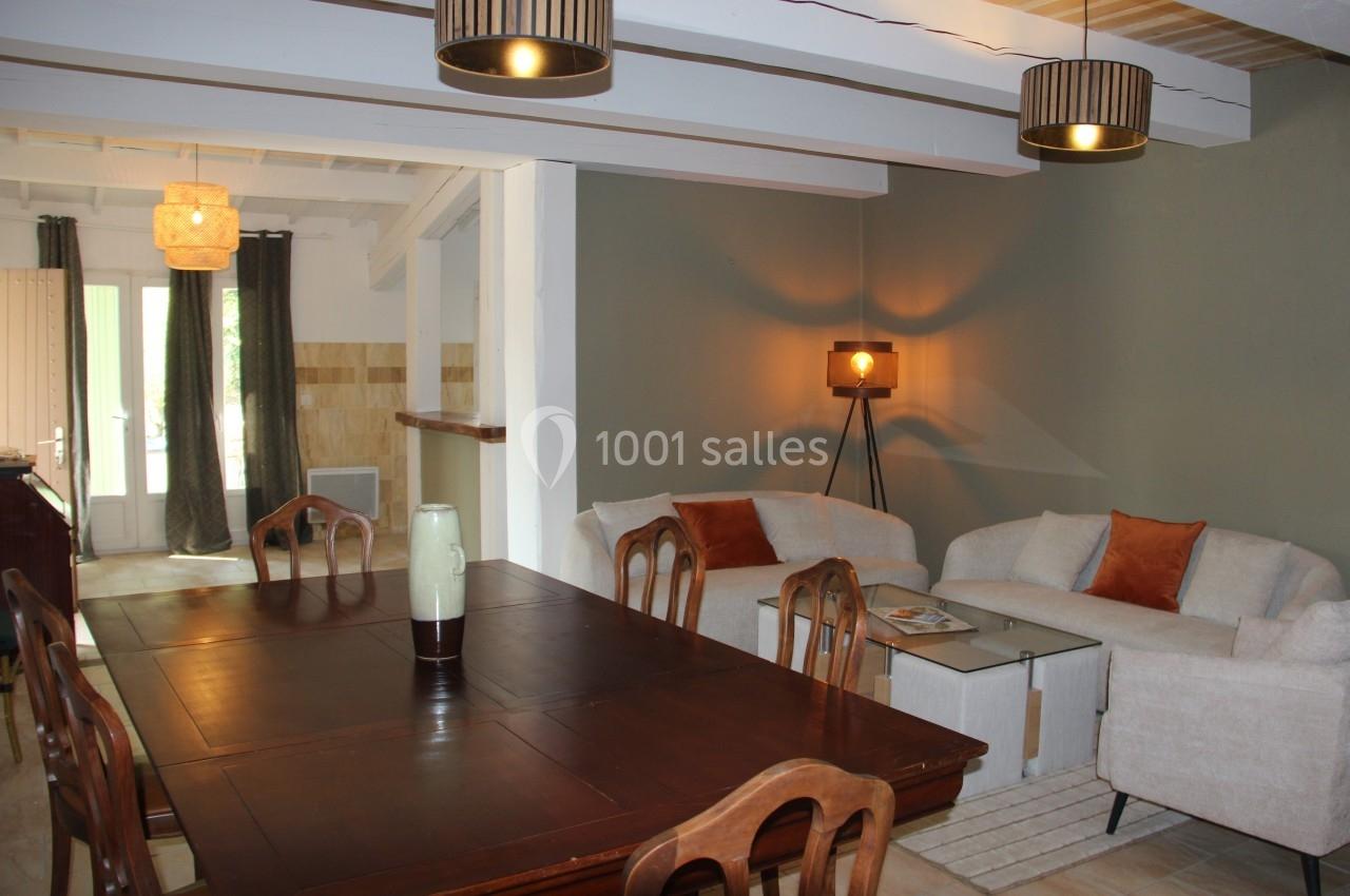 Salle à manger et salon avec table en bois, canapés clairs, lampes suspendues et lumière naturelle.