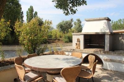 Terrasse couverte en bois avec mobilier d'extérieur blanc, donnant sur un jardin arboré et une allée gravillonnée.