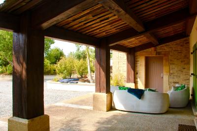 Terrasse couverte en bois avec mobilier d'extérieur blanc, donnant sur un jardin arboré et une allée gravillonnée.