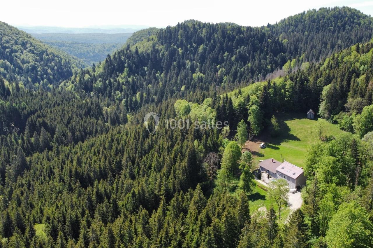 Location salle Crozets (Jura) - Domaine Le Coupet #1 Vue aérienne d'une maison isolée entourée de forêts denses et de collines verdoyantes sous un ciel dégagé.