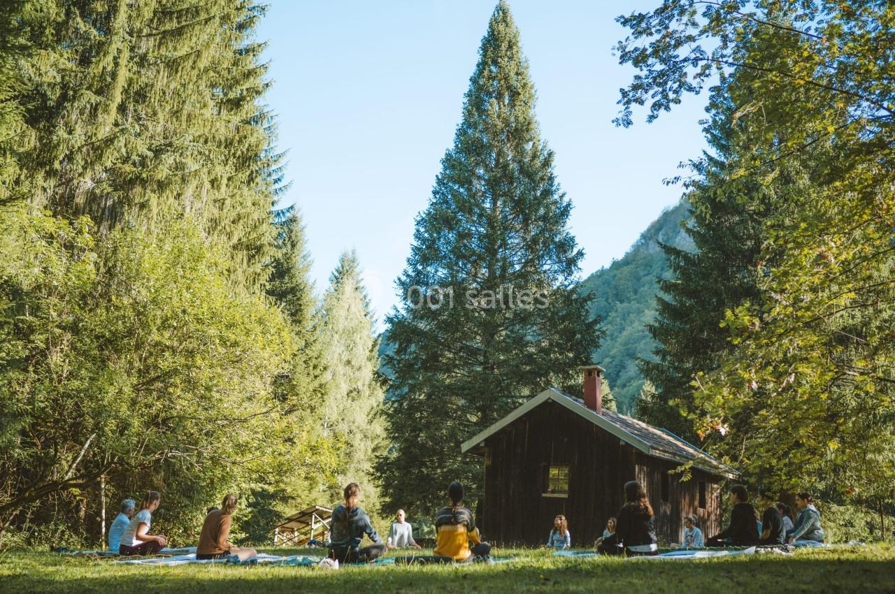 Location salle Crozets (Jura) - Domaine Le Coupet #10 Groupe de personnes assises en cercle dans une clairière boisée près d'une petite cabane en bois.