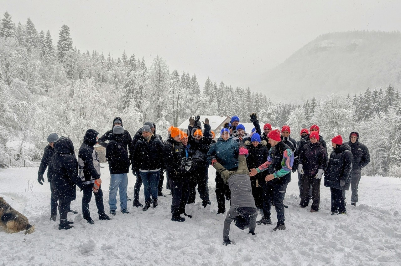 Location salle Crozets (Jura) - Domaine Le Coupet #13 Un groupe de personnes habillées chaudement pose dans un paysage enneigé avec des arbres et des collines en arrière-plan.