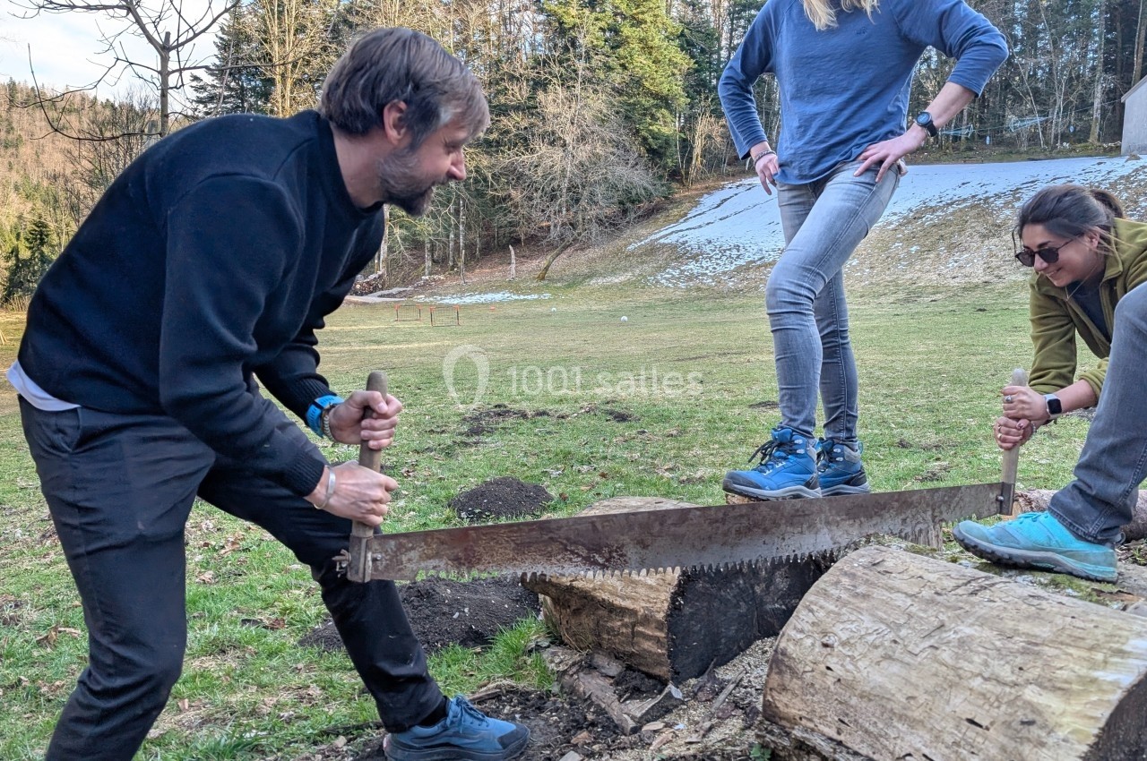 Location salle Crozets (Jura) - Domaine Le Coupet #21 Deux personnes scient un tronc d’arbre avec une grande scie, sous le regard de deux autres dans un cadre naturel.