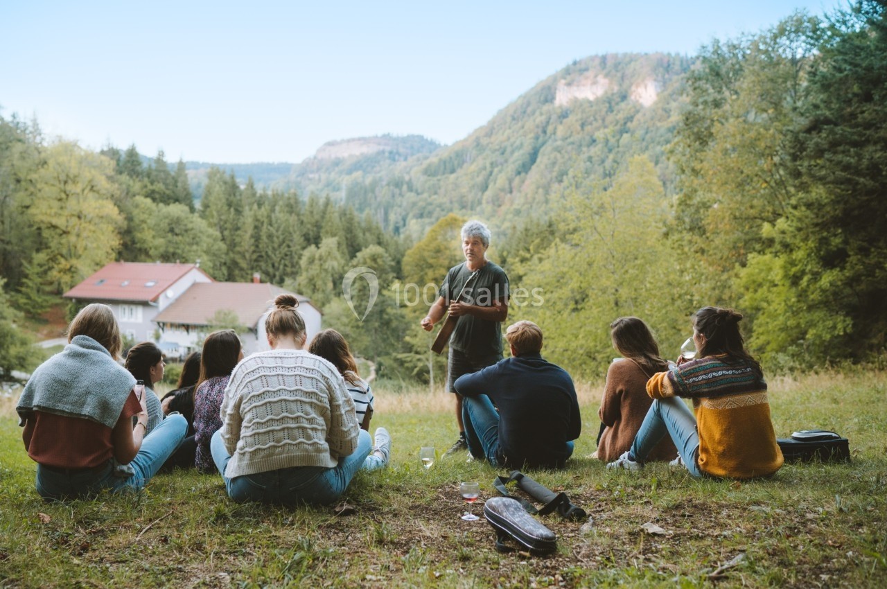 Location salle Crozets (Jura) - Domaine Le Coupet #22 Un groupe de personnes assises en cercle dans une clairière, écoutant une personne debout devant un paysage boisé.