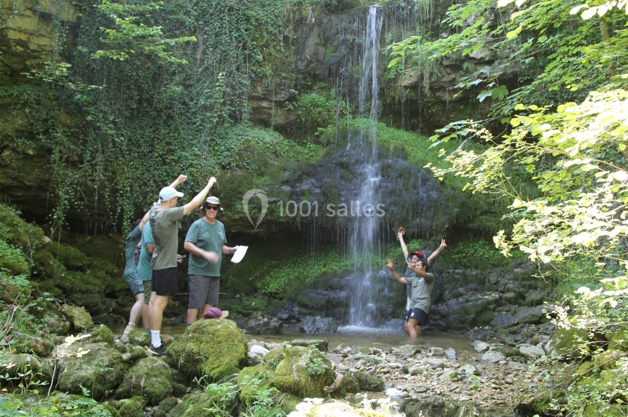 Location salle Crozets (Jura) - Domaine Le Coupet #12 Des personnes profitent d'une cascade entourée de végétation dense, l'une d'elles se tenant dans l'eau.