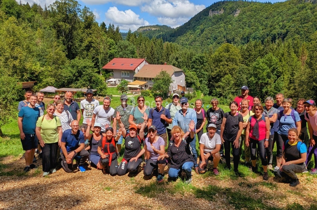 Location salle Crozets (Jura) - Domaine Le Coupet #2 Un groupe de personnes pose en extérieur devant un paysage verdoyant avec des collines et un bâtiment en arrière-plan.
